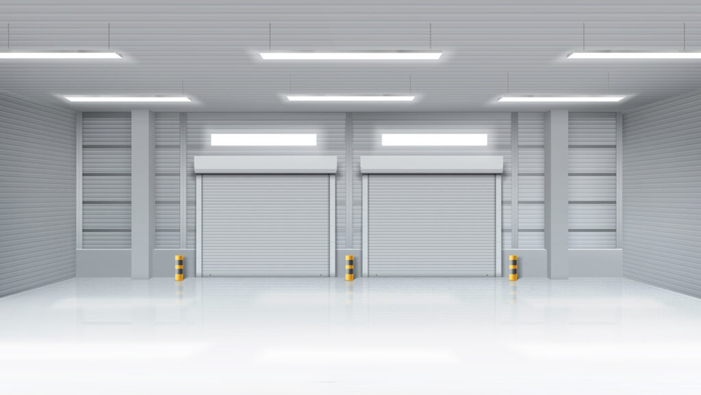 Empty industrial warehouse interior with two closed white roller shutter garage doors and yellow safety bollards, photographed in Prestons, New South Wales, Australia.